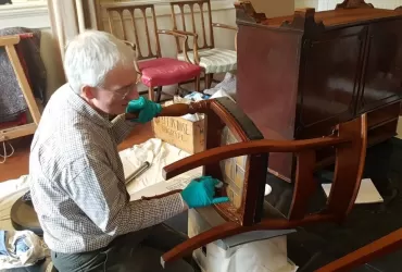 Man wearing latex gloves brushing the underside of an antique wooden chair